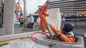 Ava Daugherty, of Juneau, grabs a pink salmon from Sara Gering, of Juneau, as the two work to offload more than 40,000 pounds of salmon from the fishing tender San Juan on July 19, 2018, in Juneau, Alaska. Bonny Millard, the captain, says it has been an unusual season for sockeye salmon in Southeast, Alaska. (Photo by Rashah McChesney/Alaska’s Energy Desk)