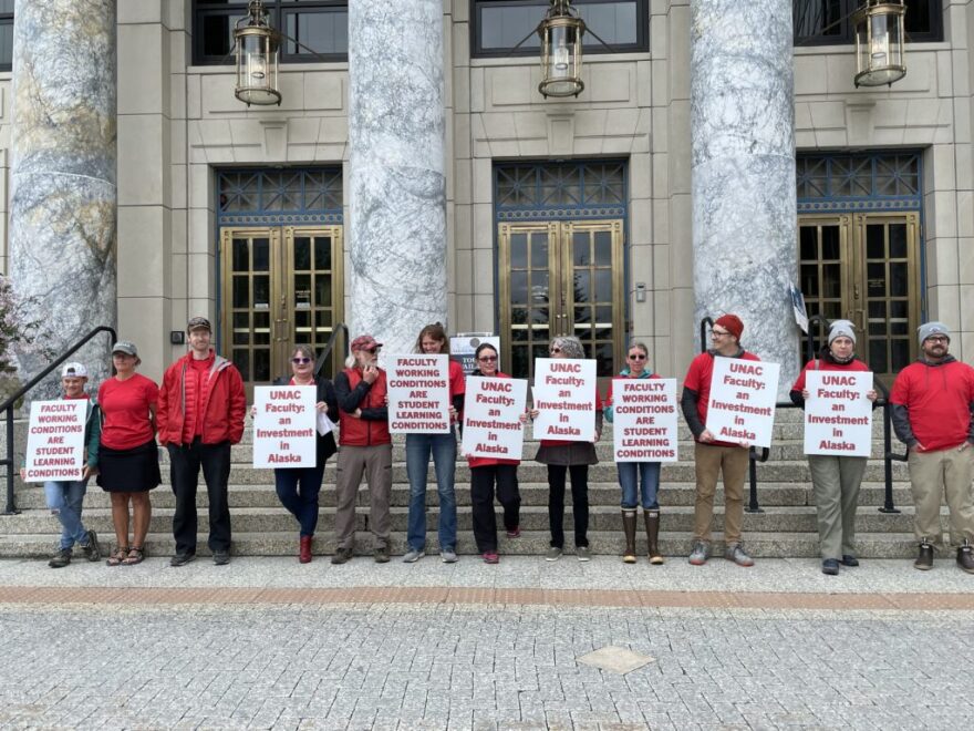 People in red stand in a line outside, holding sings that say "UNAC Faculty: an investment in Alaska"