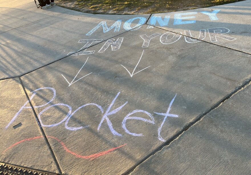 The words Money in your Pocket written in bright chalk on a paved campus walkway.
