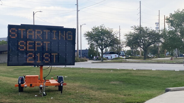 A large electronic sign on wheels placed in a grassy area next to a parking lot. The sign reads 'Starting Sept. 21st.' 