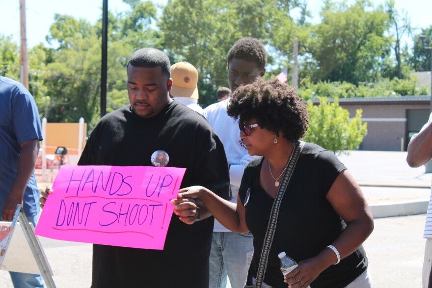 Sen. Maria Chappelle-Nadal attends a protest holding the hand of a man holding a bright pink sign that reads "HANDS UP! DONT SHOOT!"