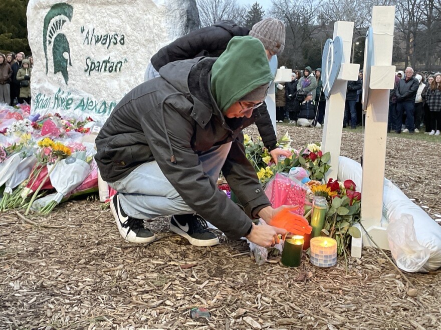 A community member cups his hands around a candle to light the wick at the student memorial. 