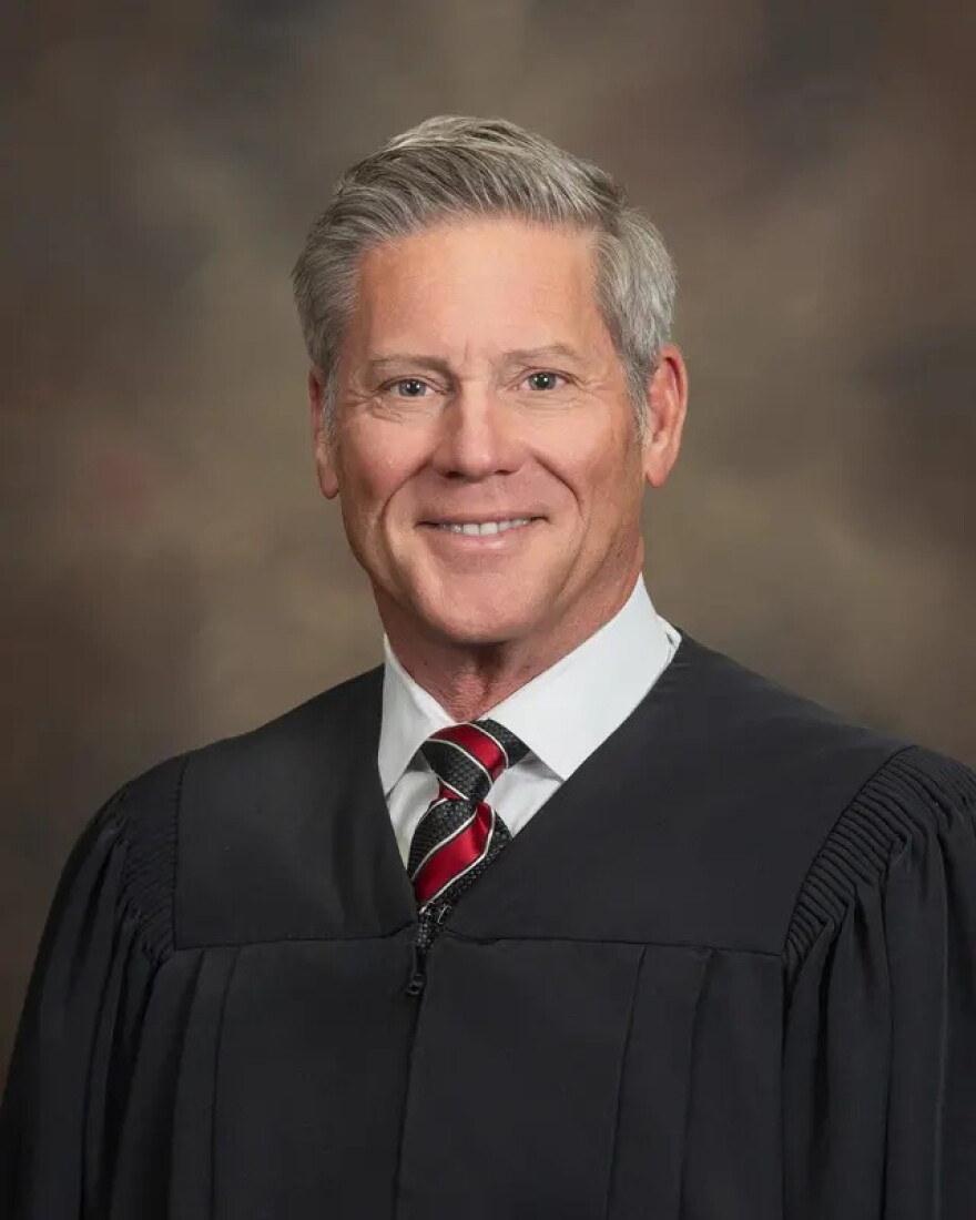 man with greying hair sits in a judge's robe