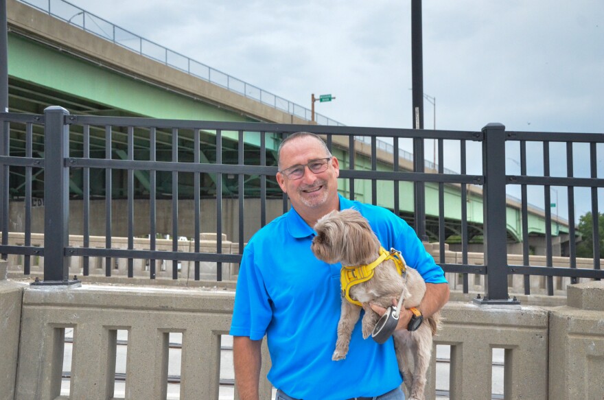 A man poses with his small dog on a bridge.