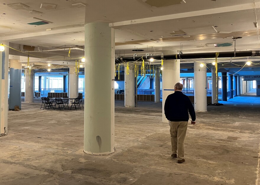  Ken Greene, director of commercial development for Sibley Square, walks through the expansive but currently empty space that will be a hallway and SWBR's new offices on the fourth floor of Sibley Square. Large concrete columns rise in a grid across the space. Temporary construction lighting is string along the exposed ceiling.