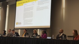 The Western Michigan University Board of Trustees sits at a long, black table, each with a microphone in front of them. The trustees are all looking off to the side, and a projector behind them shows a document titled "Agenda Item No. 13". The agenda item is for the transfer of the Asylum Lake Preserve to Kalamazoo County. 
