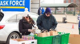A man and a woman in cold-weather clothing sort food donation outdoors with a car in the background.