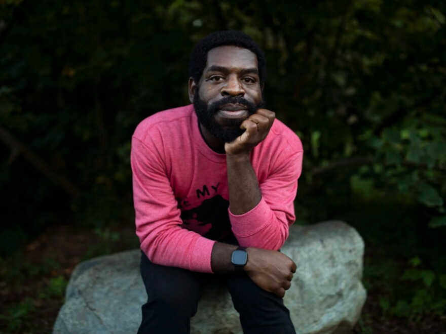 Hanif Abdurraqib sitting a boulder, propping up his chin with his hand