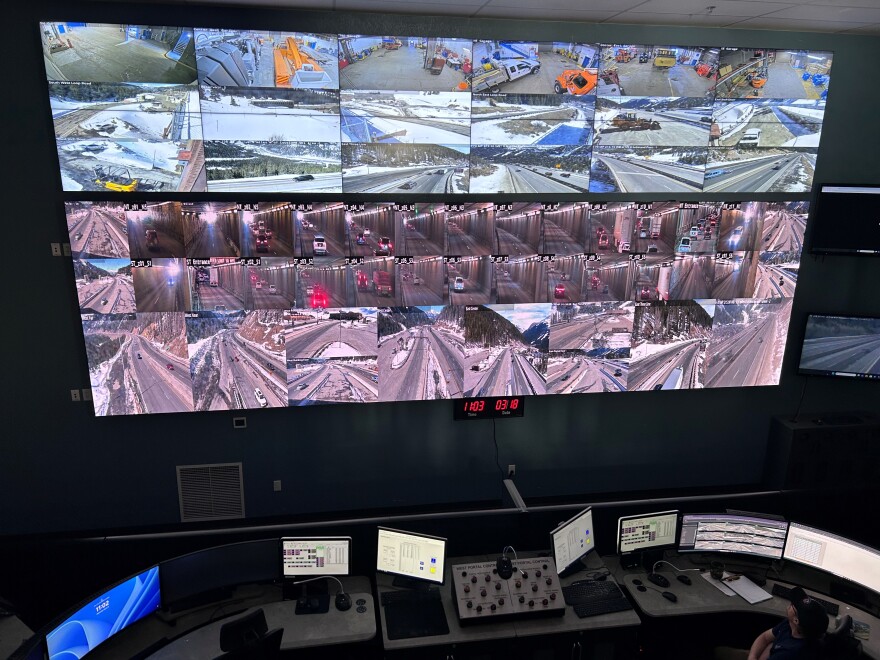 Several rows of screens with camera angles of the Eisenhower Johnson Memorial Tunnel hang on the wall. Below is a desk with some computer screens and a guy looking at them all. 