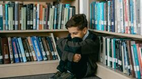 Boy sitting in a Library covering his face.