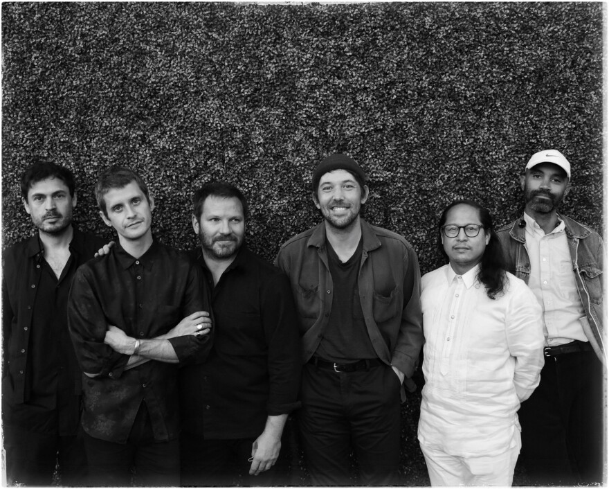 A black-and-white of members of the band the Fleet Foxes standing in front of a hedge. There are six of them. 