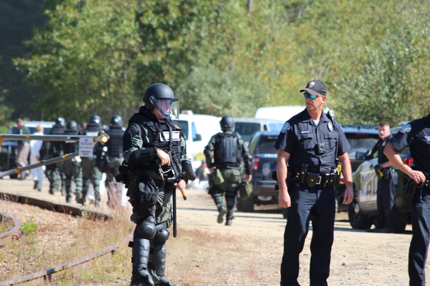 A state trooper with a paintball gun stands guard as protesters are detained outside Merrimack Station.