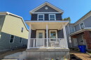 A two story home with a white porch and blue grey vinyl siding.