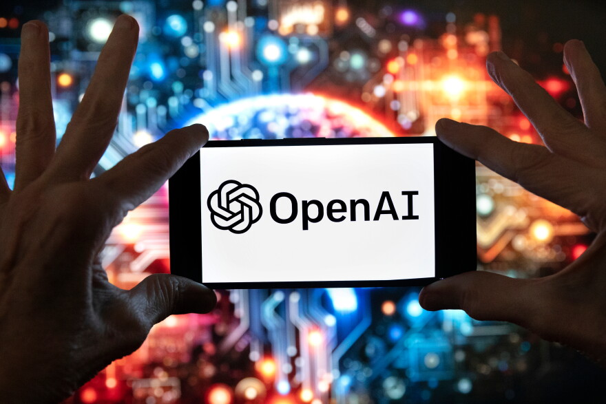 The OpenAI logo is displayed on a cell phone in front of an image generated by ChatGPT's Dall-E text-to-image model, Dec. 8, 2023, in Boston.