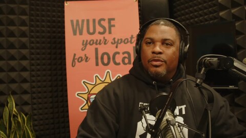 African American man sits by microphone with headphones on 