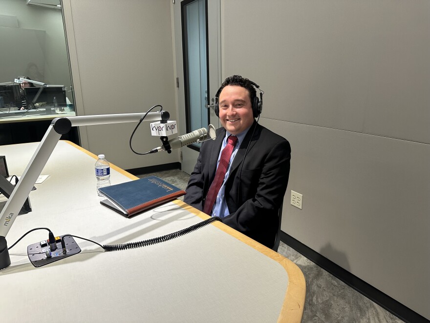 A man sits in front of a microphone for an interview with headphones on
