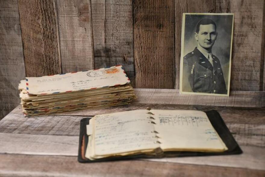 A journal and a stack of letters site on a table near a photo of a soldier