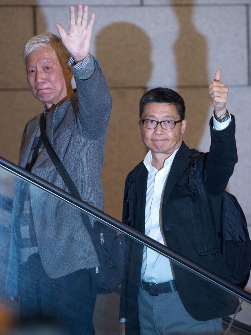 Activists Chu Yiu-ming, left, and Chan Kin-man gesture to supporters as they report to be arrested at a police station in Hong Kong. Police say the men and other Umbrella Movement activists will be charged over mass protests that took place in 2014.