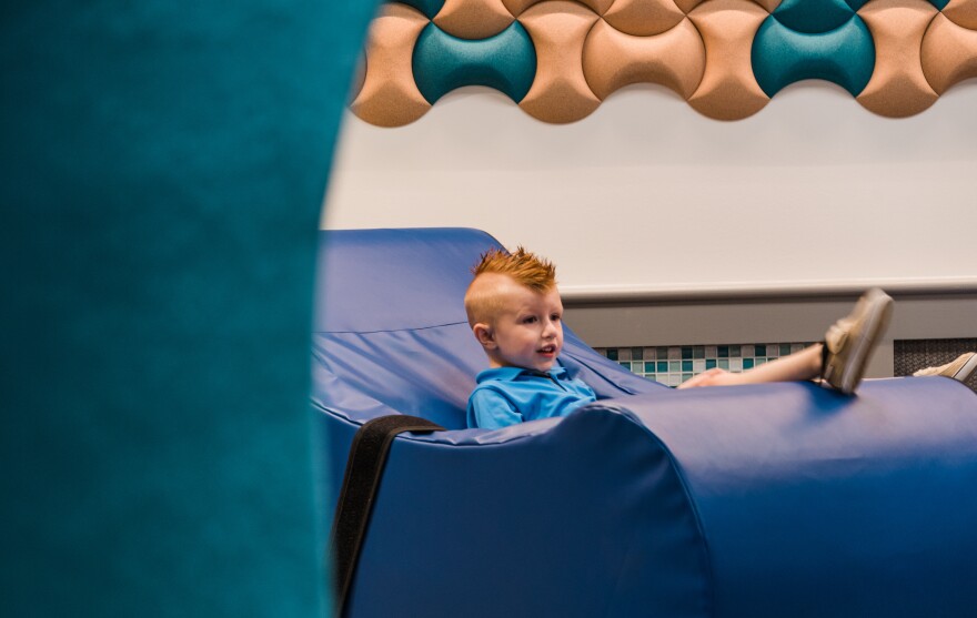 Presley Rudge, a 4-year-old with autism, tries out one of the sensory room's soft rocking chairs. The chair comes with a safety strap to prevent falls.