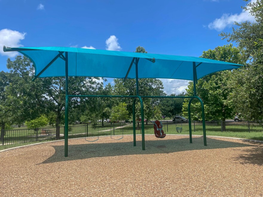 A blue mesh shade structure is draped over a green swing set at a public park in Southeast Austin. 