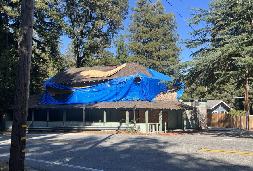 A dilapidated building is covered in a large blue tarp, and its windows are all boarded up.