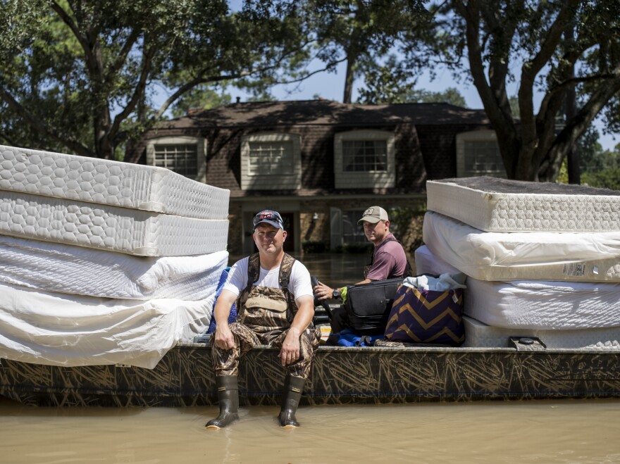 Scott McKnight (left) rides in a boat with his mattresses in the Nottingham Forrest subdivision of Houston on Thursday. Bret Hinkie, a Houston-area commercial airline pilot and a high school friend of McKnight, is volunteering to drive residents to their homes in his boat.