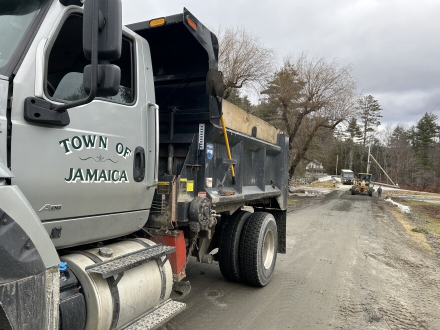 A road crew truck that reads "town of Jamaica" works on a damaged road after the December floods.