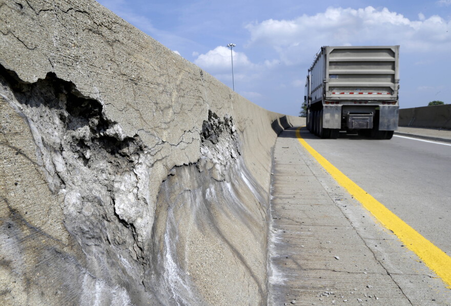 a dump truck drives past cracked and broken concrete on bridge barrier