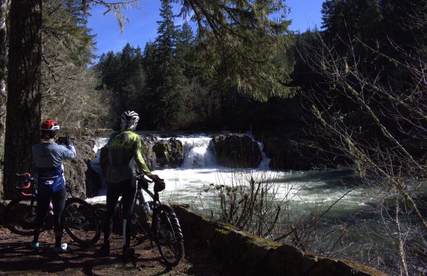 Two bicyclists on a path stop take a photo of a waterfall