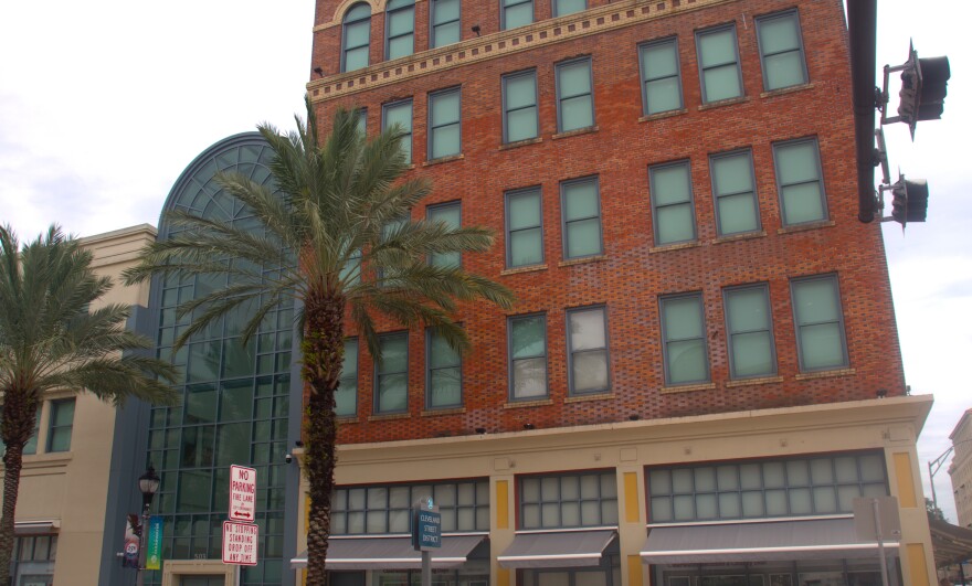 Multi-story brownstone building with dozens of windows. There are palm trees in front of it.