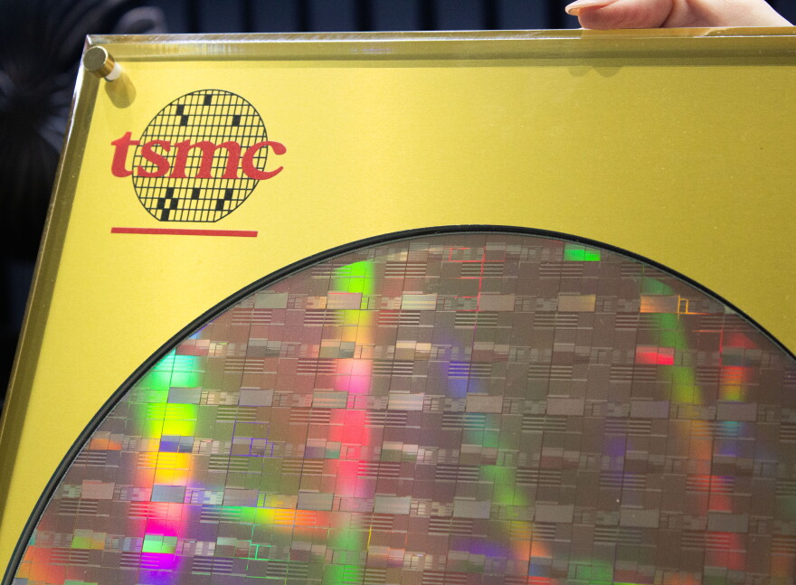 A silicon wafer made by TSMC is in a frame with a golden backing and a logo for TSMC in the top left corner. The wafer is a 12 inch diameter piece of silicon that has the chips that will eventually be put into computers, phones, or other products. 