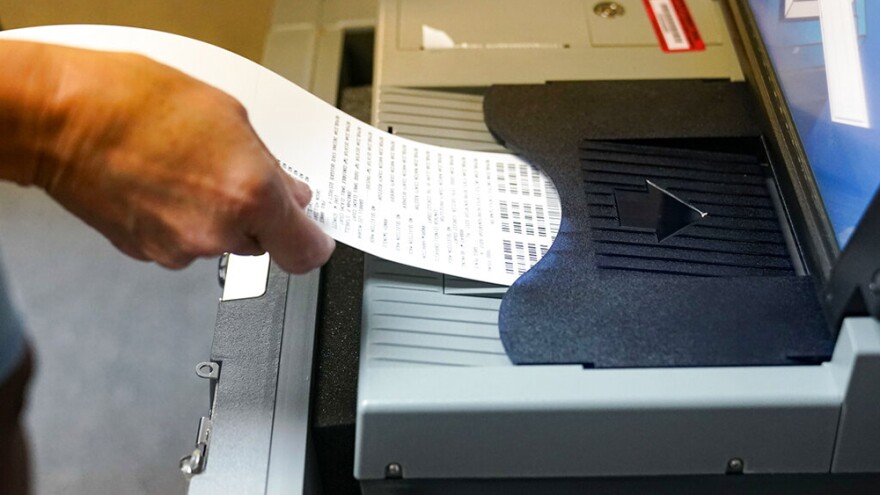 A voter inserts her ballot into a scanner as she votes in the primary election in Indianapolis, Tuesday, May 3, 2022.