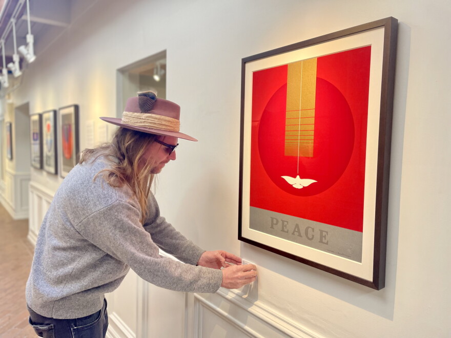 Fat City Gallery Director D.J. Watkins adjusts a label on the wall beneath a Thomas W. Benton silkscreen print with “Peace” iconography at the gallery’s newest location on Feb. 7. 