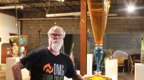 A man in a black t-shirt poses with a giant art sculpture made of glass