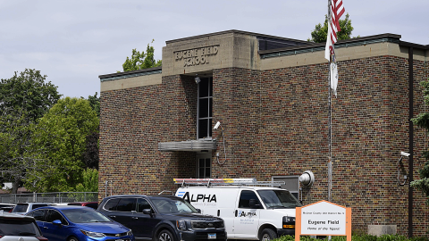 A view of a brick building from the outside. Cars are parked out front.