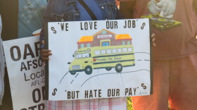 Close-up of a Princeton bus driver holding a sign that reads "We love our job, but hate our pay."