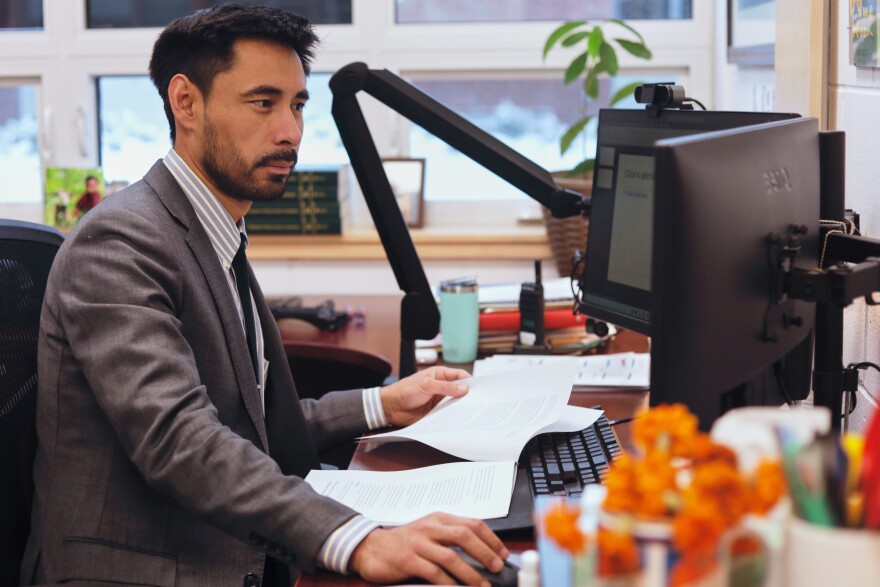 A man in a suit sits at his desk