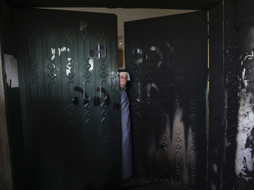 A Palestinian man stands on the doorway of a burned mosque in the West Bank village of Deir Istiya, on Wednesday.