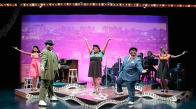 Five Black actors on stage for a musical revue. They are wearing 1920's era fashion. A piano and musicians appear in background.