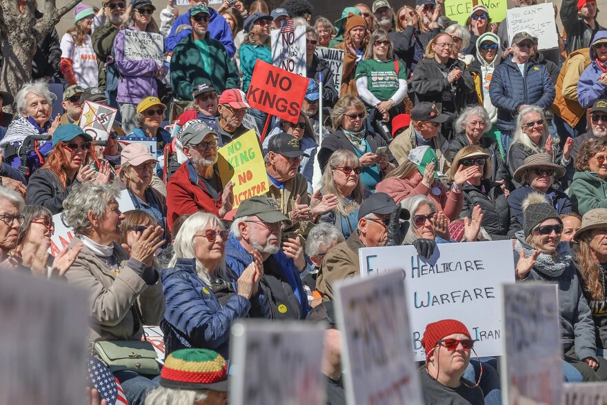 A crowd of protestors clap hands and hold signs that voice displeasure with President Donald Trump's governing practices.