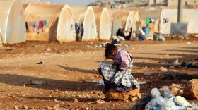 A girl writes in a notebook as she sits outside a tent at the Furat (Euphrates) camp for the displaced from Deir Ezzor, north of the town of Kafr Dariyan in the countryside of the northern province of Idlib.