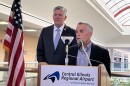 A tall man in a suit with a congressional pin, U.S. Rep. Darin LaHood stands next to a short man, Central Illinois Regional Airport Board Chair Alan Sender, at a lectern with a regional airport placard on the front of the lectern. 