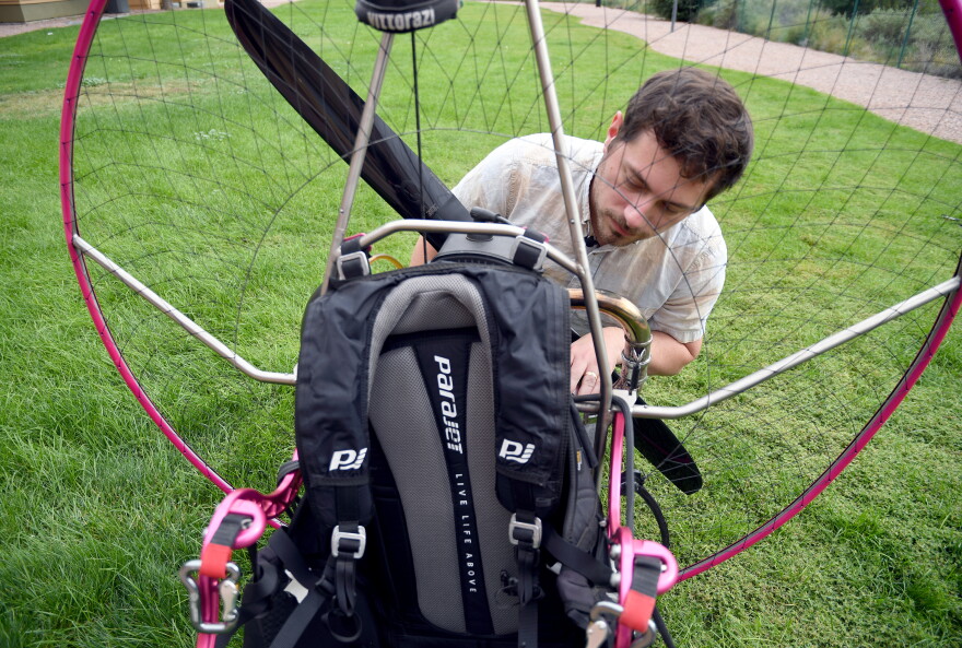 Jake Hutzler inspects his paramotor backpack while standing on a grassy lawn.