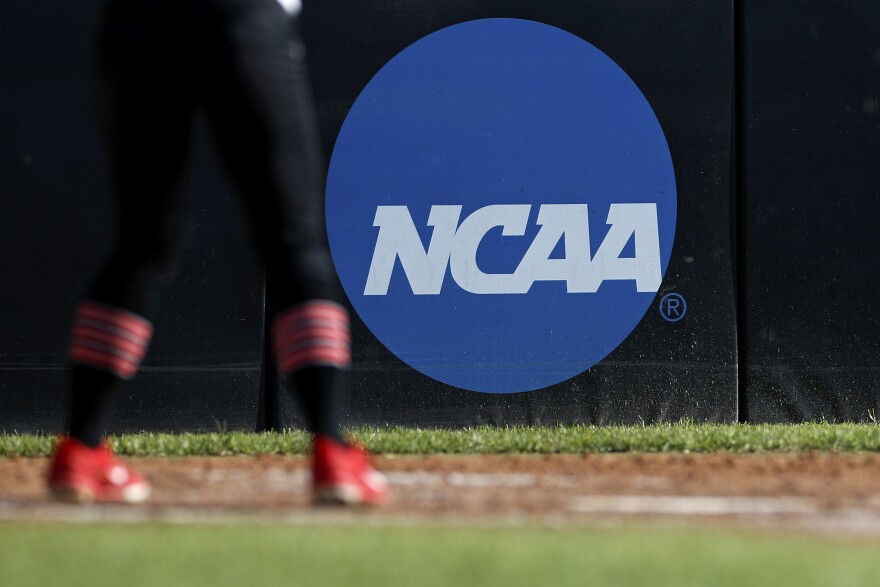 In this April 19, 2019, file photo, an athlete stands near a NCAA logo during a softball game in Beaumont, Texas. The NCAA is poised to take a significant step toward allowing college athletes to earn money without violating amateurism rules.