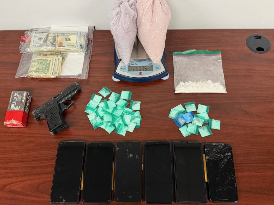 money, drugs, cell phones and a gun seized by police in a drug bust are laid out on an office desk.