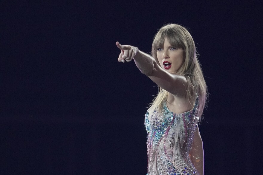 a blonde woman in a sparkly bodysuit points to out to the crowd