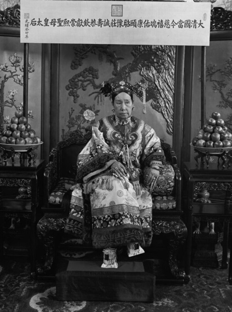 This photograph is one of a series of photos that shows Cixi seated on her throne in front of a banner that declares her full title. <a href="http://media.npr.org/assets/artslife/arts/2011/12/cixishoes_custom.jpg">Click here to see a close-up</a> of her "horse-hoof" platform shoes.