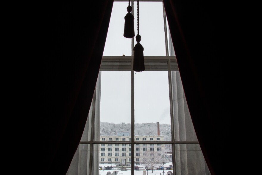 Dark curtains obscure a view out a window of a building covered in snow.