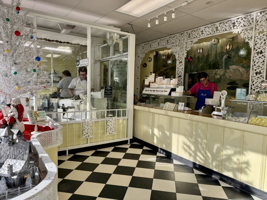 A small candy shop with black and white checkered floor and a woman behind the counter.