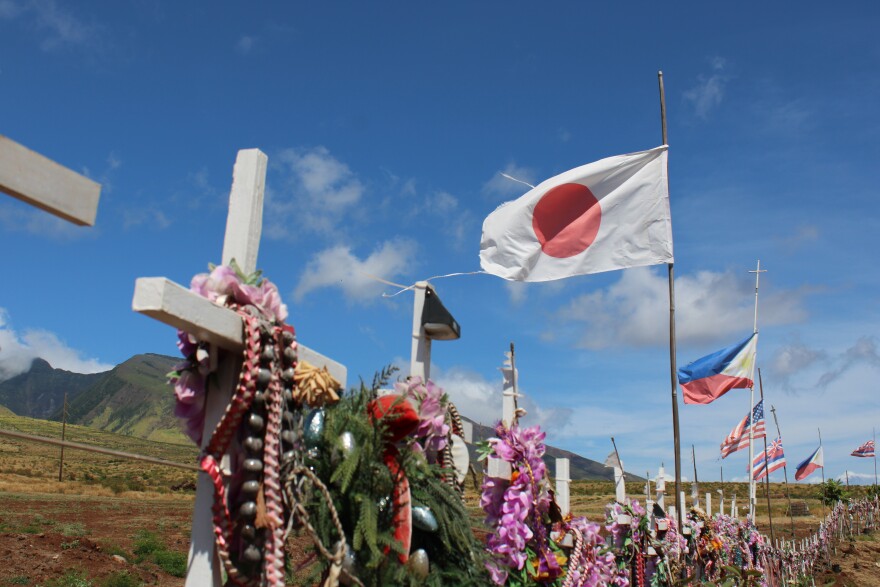 An image of a memorial near the Lahaina Bypass highway that includes a cross and a photo of each of the August 2023 wildfire victims.
